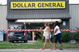 Two women walk by the Dollar General store, which is cordoned off with police tape following a shooting incident.