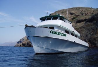 The Conception boat anchored near coastal cliffs, identified by its name on the hull.