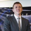 A man in a suit stands in front of a Project Veritas banner, appearing confident during a public event. A man in a suit stands in front of a Project Veritas banner, appearing confident during a public event.