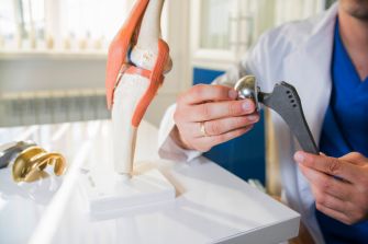 A medical professional demonstrating a hip implant attachment using a model of a knee joint.