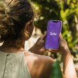A woman holding a smartphone displaying the Zelle app logo, surrounded by greenery. A woman holding a smartphone displaying the Zelle app logo, surrounded by greenery.