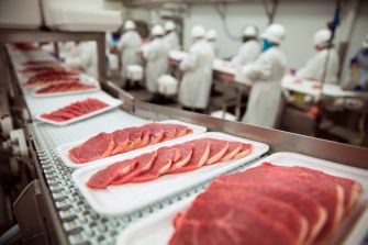 Pork products being processed in a meatpacking facility, with workers in protective attire in the background.