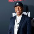 Russell Simmons smiling at a public event, wearing a baseball cap and suit. Russell Simmons smiling at a public event, wearing a baseball cap and suit.