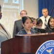 A woman speaks at a podium during a press conference addressing criminal charges against contractors involved in a fatal construction site accident. A woman speaks at a podium during a press conference addressing criminal charges against contractors involved in a fatal construction site accident.