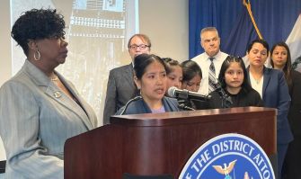 A woman speaks at a podium during a press conference addressing criminal charges against contractors involved in a fatal construction site accident.