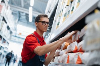 A warehouse employee in a red shirt organizing products on a shelf in a supermarket distribution center.