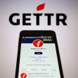 Logo of GETTR with a smartphone displaying the support account on the platform. Logo of GETTR with a smartphone displaying the support account on the platform.