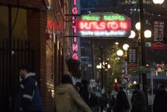 Neon sign for Union Gospel Mission in Seattle, with individuals walking past in the evening.