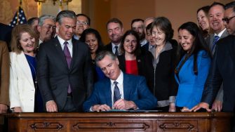 Governor Newsom signing legislation surrounded by supporters in a formal setting.