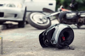 A motorcycle helmet on the ground near an accident scene, with a car and motorcycle in the background.