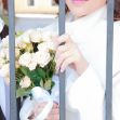 A woman in a white coat holding a bouquet of roses, standing behind metal bars, with a man in a suit beside her. A woman in a white coat holding a bouquet of roses, standing behind metal bars, with a man in a suit beside her.