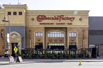 Exterior view of a Cheesecake Factory restaurant featuring outdoor seating and signage.