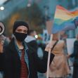 A person holding a megaphone and a rainbow flag at a rally, surrounded by a crowd. A person holding a megaphone and a rainbow flag at a rally, surrounded by a crowd.