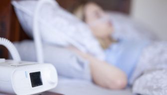 Close-up of a breathing machine next to a person asleep in bed.