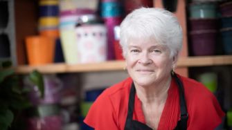A florist posing in her shop, surrounded by colorful flower containers.