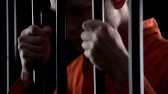 A close-up of a person in an orange prison jumpsuit holding onto prison bars.