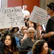 A crowd attending a meeting, with individuals holding signs supporting LGBTQ+ rights and advocating for the protection of queer and trans youth. A crowd attending a meeting, with individuals holding signs supporting LGBTQ+ rights and advocating for the protection of queer and trans youth.