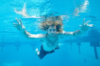 A man with long hair swimming underwater, reaching out with his hands.