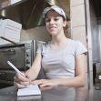 A young female worker taking orders in a restaurant kitchen setting. A young female worker taking orders in a restaurant kitchen setting.