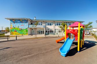 Playground and school building with a colorful slide and murals in the background.