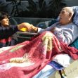 A woman and a man in a hospital bed share a moment together, with the man covered by a colorful blanket. A woman and a man in a hospital bed share a moment together, with the man covered by a colorful blanket.