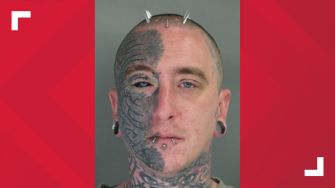 Image of a man with extensive facial tattoos and piercings, looking directly at the camera.