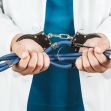 A person in a doctor's coat holding a stethoscope attached to handcuffs. A person in a doctor's coat holding a stethoscope attached to handcuffs.