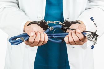 A person in a doctor's coat holding a stethoscope attached to handcuffs.