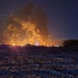 Night view of smoke and flames rising from a train derailment site in Palestine, Ohio, with an illuminated landscape. Night view of smoke and flames rising from a train derailment site in Palestine, Ohio, with an illuminated landscape.