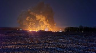 Night view of smoke and flames rising from a train derailment site in Palestine, Ohio, with an illuminated landscape.