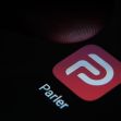 Image of the Parler app logo on a smartphone screen with a finger hovering above it. Image of the Parler app logo on a smartphone screen with a finger hovering above it.