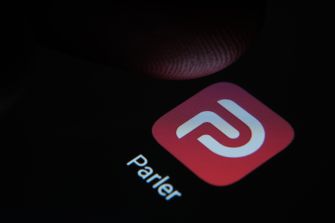 Image of the Parler app logo on a smartphone screen with a finger hovering above it.