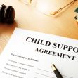 A child support agreement document with a gavel, glasses, and a book in the background. A child support agreement document with a gavel, glasses, and a book in the background.