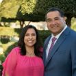 A man and woman pose for a portrait in a garden setting, smiling at the camera. A man and woman pose for a portrait in a garden setting, smiling at the camera.