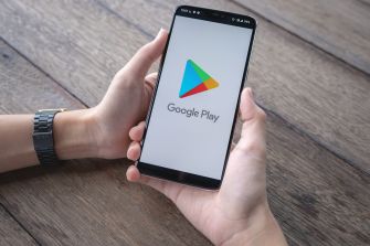 A person holding a smartphone displaying the Google Play logo on a wooden surface.