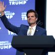A man in a suit waves while standing at a podium with a "Students for Trump" backdrop. A man in a suit waves while standing at a podium with a "Students for Trump" backdrop.