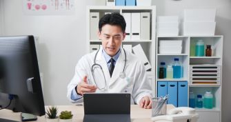A doctor in a white coat engaging in a telemedicine consultation using a tablet in an office setting.