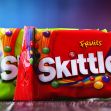 Packaging of Skittles candy in various colors displayed on a wooden surface. Packaging of Skittles candy in various colors displayed on a wooden surface.