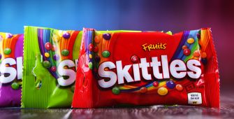 Packaging of Skittles candy in various colors displayed on a wooden surface.