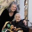 A woman poses with an elderly person outdoors, both smiling. A woman poses with an elderly person outdoors, both smiling.