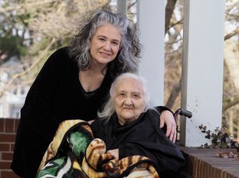A woman poses with an elderly person outdoors, both smiling.