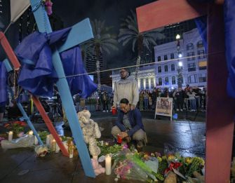 A group of women gather in a crowd, appearing emotional and supportive as they observe a memorial in New Orleans.