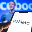 A person holding a smartphone displaying the Meta logo, with a blurred background of a man speaking at an event. A person holding a smartphone displaying the Meta logo, with a blurred background of a man speaking at an event.