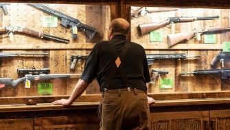 A person looking at a display of firearms in a shop.