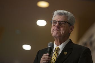 Former Mississippi Governor Phil Bryant speaking at an event, with a serious expression and microphone in hand.