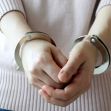 A person's hands in handcuffs, wearing a light pink sweater. A person's hands in handcuffs, wearing a light pink sweater.