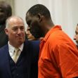 R. Kelly in an orange prison jumpsuit, accompanied by legal representatives in a courtroom setting. R. Kelly in an orange prison jumpsuit, accompanied by legal representatives in a courtroom setting.
