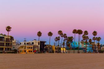 Venice, California beach scene at sunset with palm trees and colorful buildings.