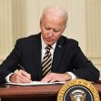President Joe Biden signing a document at a desk with the presidential seal. President Joe Biden signing a document at a desk with the presidential seal.