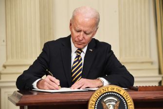 President Joe Biden signing a document at a desk with the presidential seal.